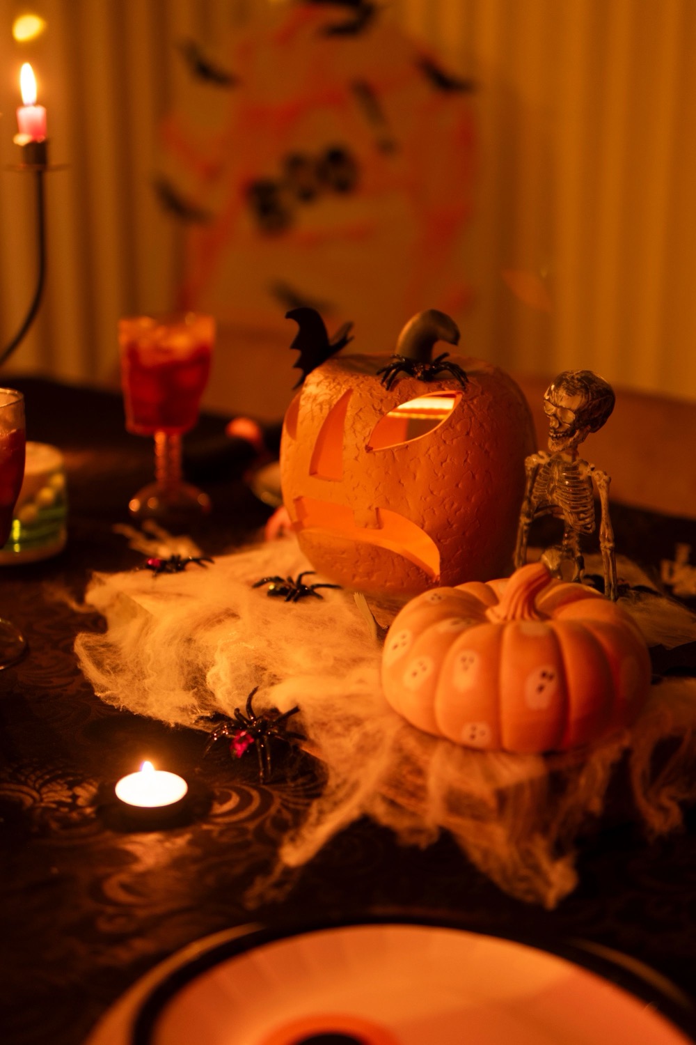 A glowing carved jack-o’-lantern beside lit candles and cobwebs on a Halloween party table